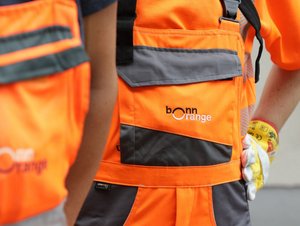 Tag der Daseinsvorsorge Zwei Mitarbeitende der bonnorange AöR in Arbeitskleidung mit den Hände mit Arbeitshandschuhen in den Hüften, der Vordergrund ist unscharf.